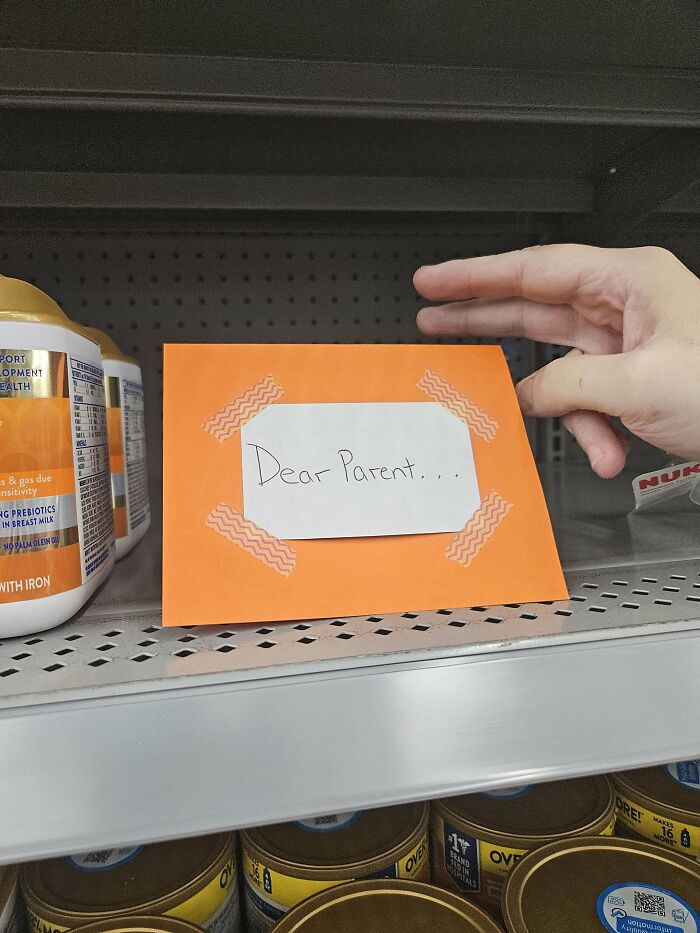 Hand holding orange envelope with a note saying dear parent found among historical mementos on a store shelf.