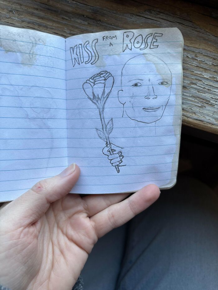 Hand holding a small notebook with a pencil drawing of a face and a hand holding a rose, a historical memento found.