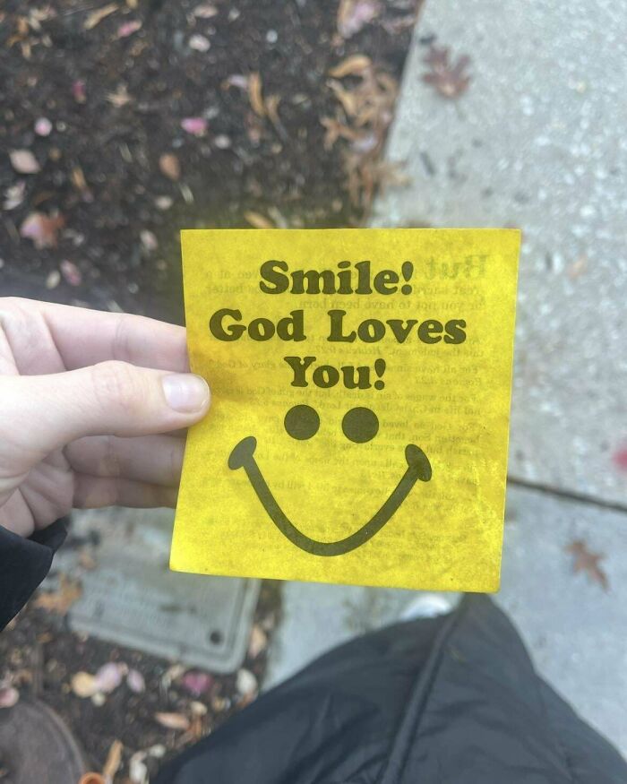 Hand holding a yellow vintage smiley face note with the message God Loves You, a historical memento found outdoors.