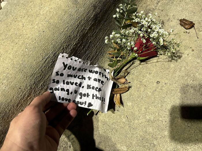 Hand holding a note with encouraging words beside a rose and small white flowers, historical mementos people found.