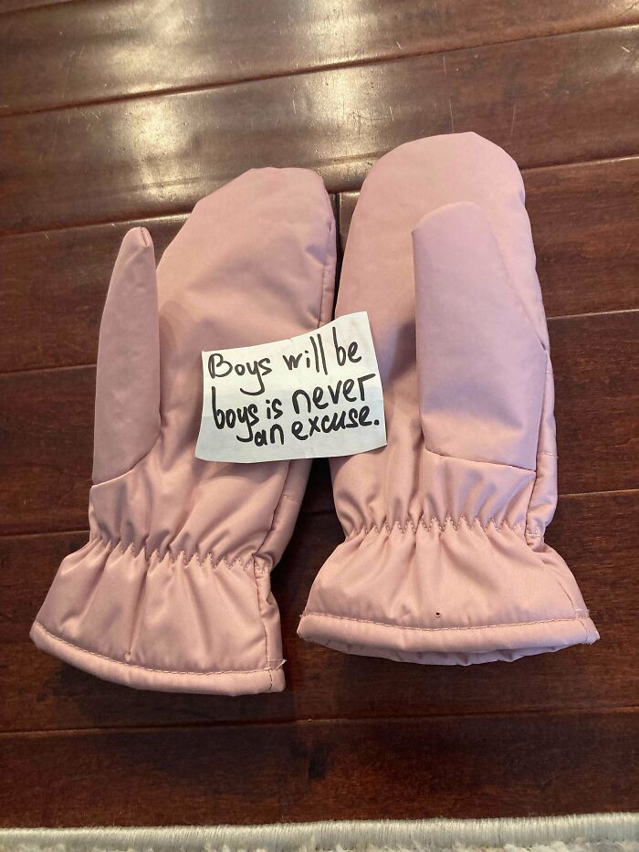 Pair of vintage pink mittens on a wooden floor with a note saying boys will be boys is never an excuse, historical memento found.