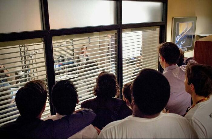 Group of people observing through window blinds, capturing photos from alternative angles in an unseen setting.