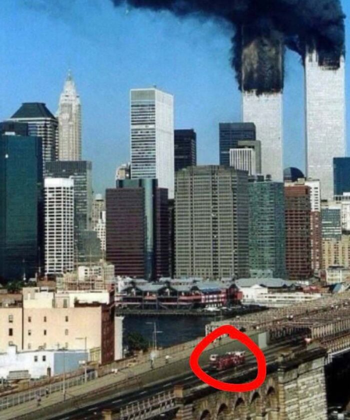 Historic photo of New York City skyline with Twin Towers burning and emergency vehicles highlighted on bridge in foreground.