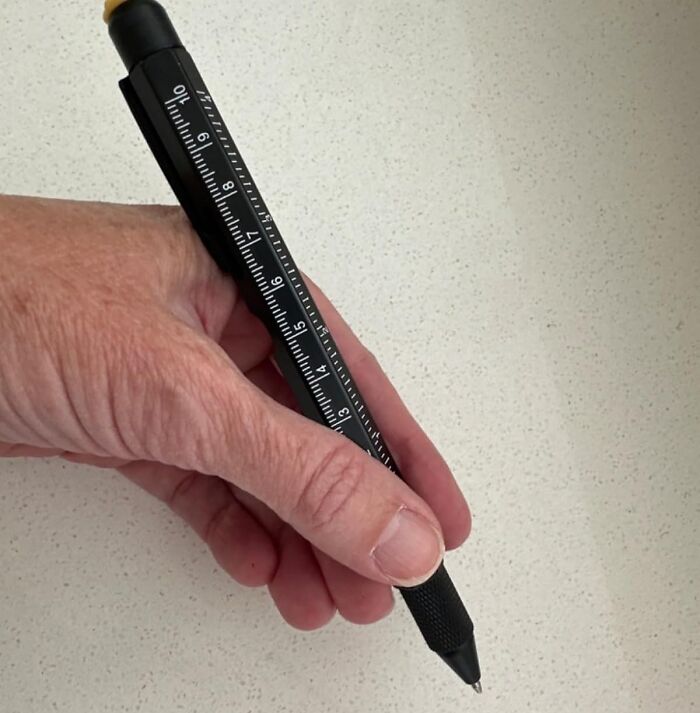 Hand holding a multi-tasking pen with built-in ruler, showcasing a versatile tool like a Swiss Army knife for home use.