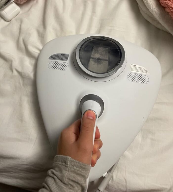 Hand holding a multi-tasking home device that resembles a Swiss Army knife on a white fabric surface.