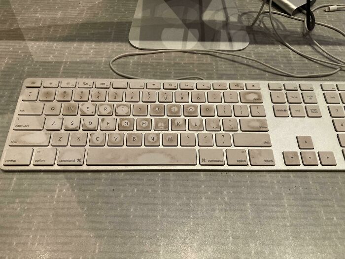 Dusty computer keyboard on a desk with tangled cables, highlighting neglect in a workspace environment.