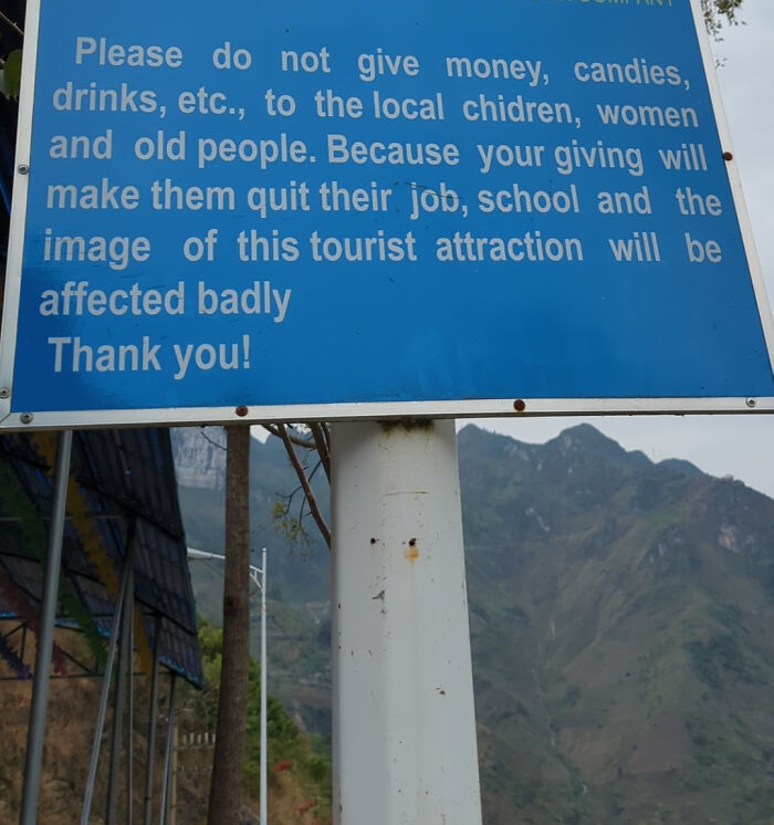 Blue sign warning tourists not to give money to local children or women to avoid traumatizing the next generation at attraction.