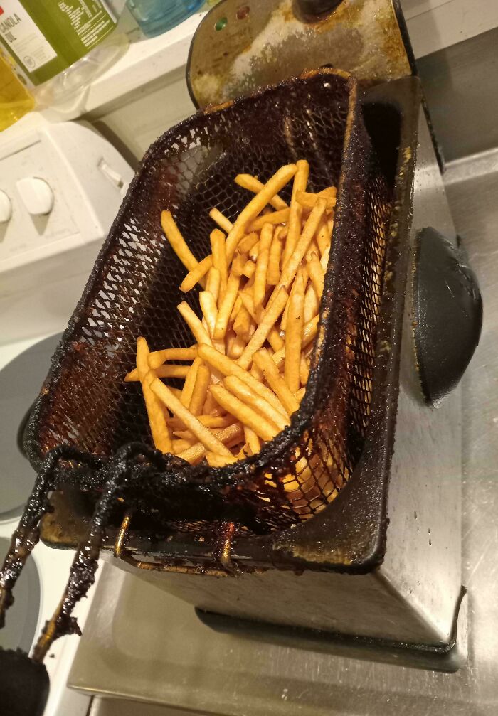 Deep fryer basket filled with freshly cooked french fries in a kitchen, showing food preparation and cooking process.