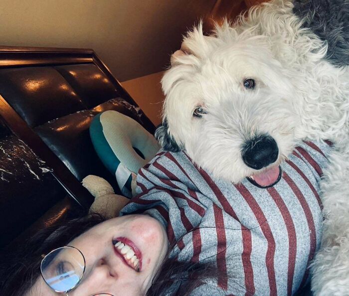 Person lying on bed smiling next to a fluffy white dog, capturing a wholesome adoption moment as new addition to the family.