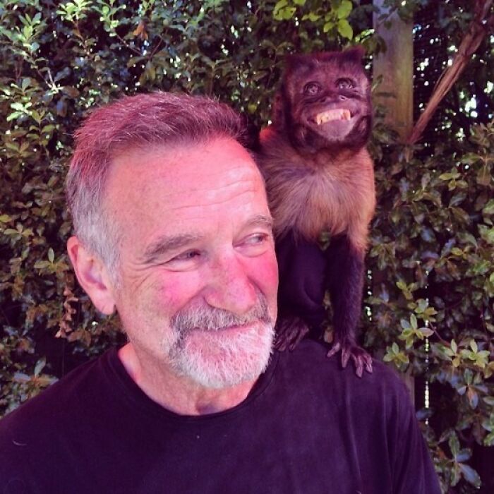Man with a beard smiling with a small monkey on his shoulder surrounded by green foliage in last known photos of famous people.