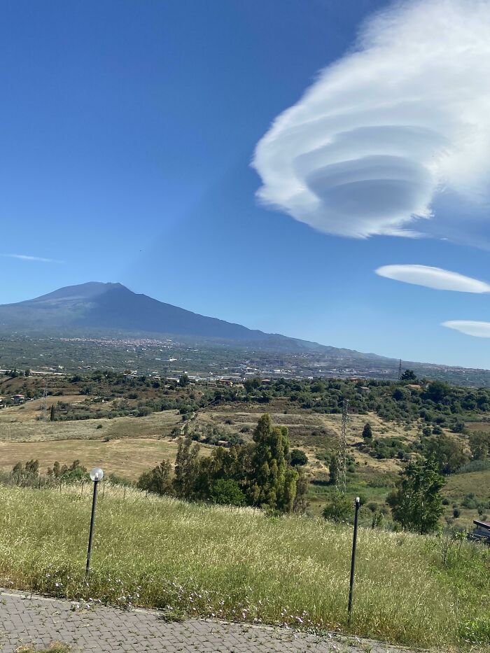 Lenticular clouds casting bizarre shadows over a rural landscape with mountains and green fields in the background.
