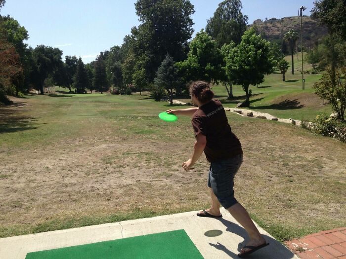 Man throwing a frisbee on a sunny day with a circular shadow appearing on the ground creating an interesting shadow effect