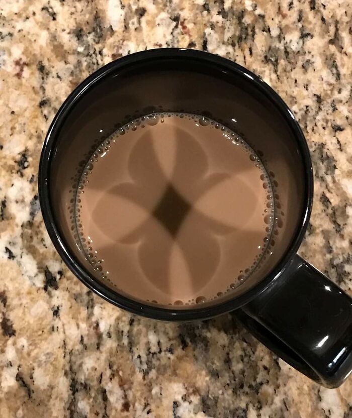Shadow in coffee forming a cool and interesting symmetrical flower shape inside a black mug on granite countertop