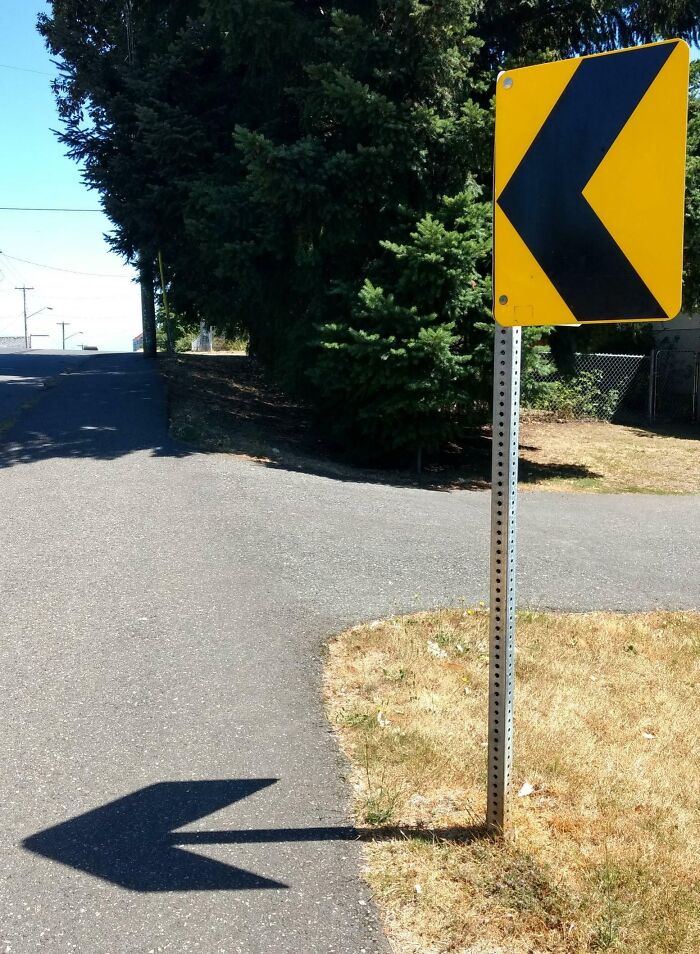 Shadow of a road sign creating a cool and interesting arrow shape on the pavement, showcasing bizarre shadows effect.