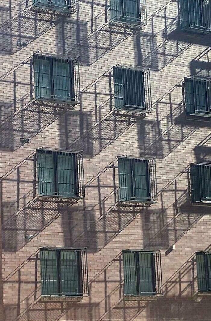 Shadows cast by window grates create cool and interesting patterns on a brick building facade in bright sunlight.