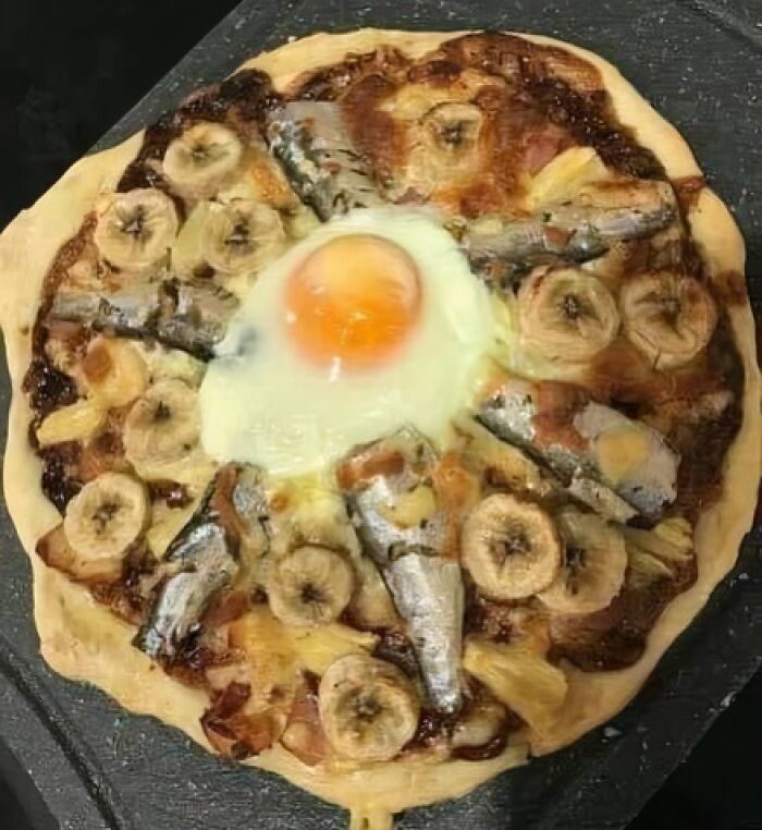 Pizza topped with fried egg, banana slices, pineapple chunks, and whole fish, an example of gross foods that may lose your appetite.