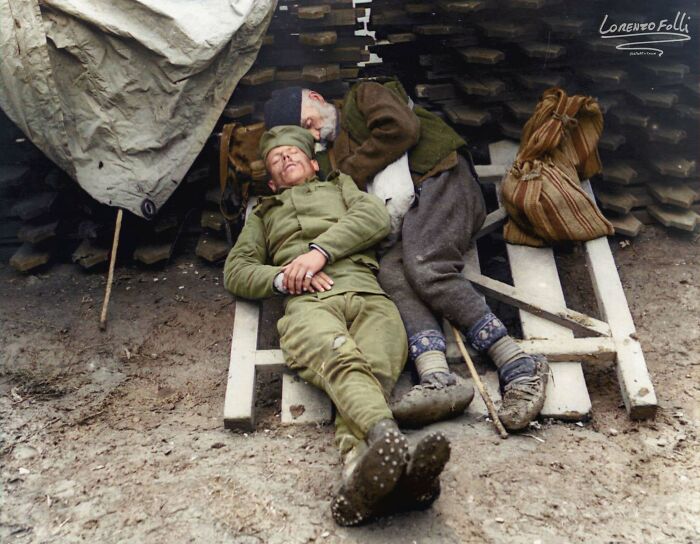 Two soldiers resting on wooden pallets in a muddy area, showcasing interesting colorized history pics from wartime.