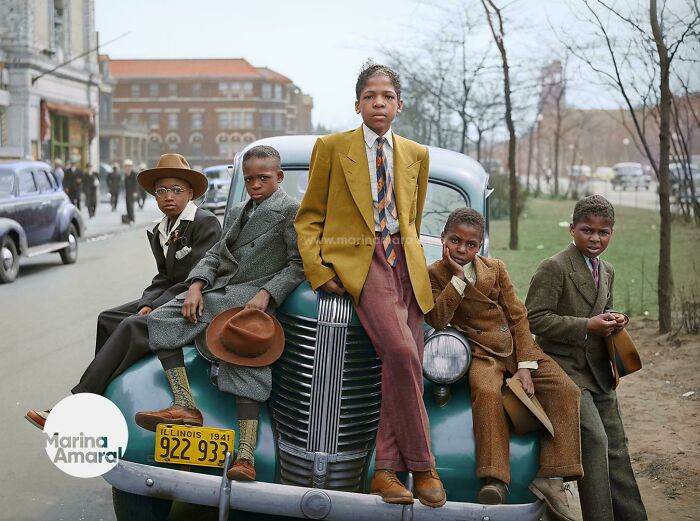 Five boys dressed in vintage suits posing on a classic car in an interesting colorized history pics photo.
