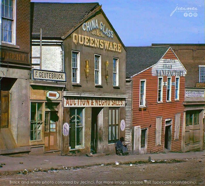 Colorized history image showing old storefronts including China Glass Queensware and auction sales on a dusty street.