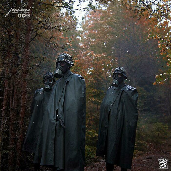 Three soldiers wearing gas masks and dark raincoats stand in a forest with autumn foliage in interesting colorized history pics.
