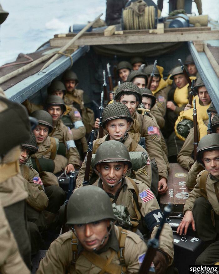 Group of soldiers in helmets and uniforms sitting closely inside a military vehicle in an interesting colorized history pic.