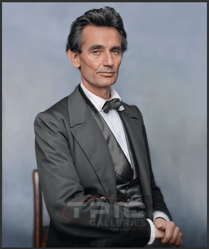 Colorized history pic of Abraham Lincoln seated, wearing a black suit and bow tie, looking directly at the camera.