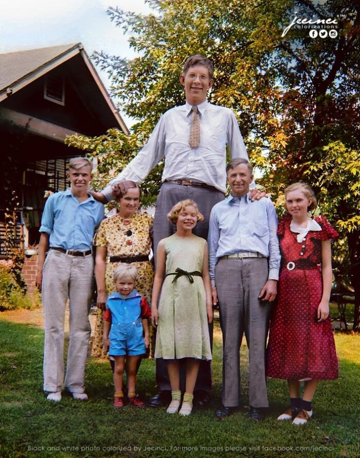 Tall man standing with smiling family in a garden, an interesting colorized history pics showing vintage clothing and setting.