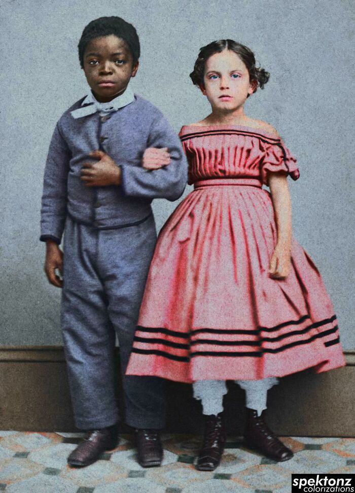 Two children from the 19th century posed together in colorized history pics, wearing period clothing and sturdy boots.