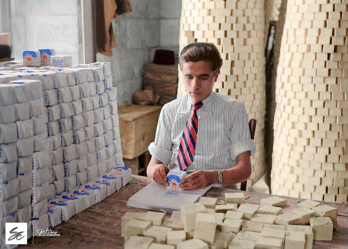 Young man packaging soap bars in a factory surrounded by stacks of soap in interesting colorized history pics.