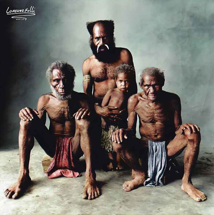 Colorized history pic showing four indigenous men and a child in traditional attire posed against a simple background.