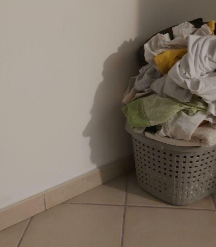 Shadow resembling a face cast on a wall by a laundry basket filled with clothes, showcasing a cool and interesting shadow effect.