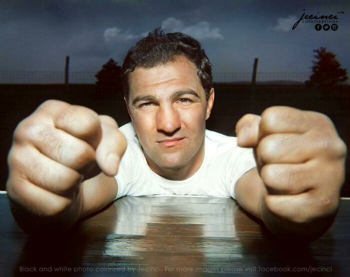 Colorized history pic of a man with clenched fists leaning forward, showcasing an intense expression and vintage setting.