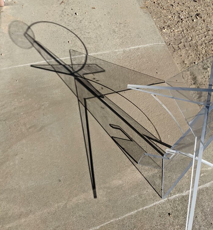 Abstract geometric sculpture casting cool, interesting, and bizarre shadows on concrete ground in bright sunlight.
