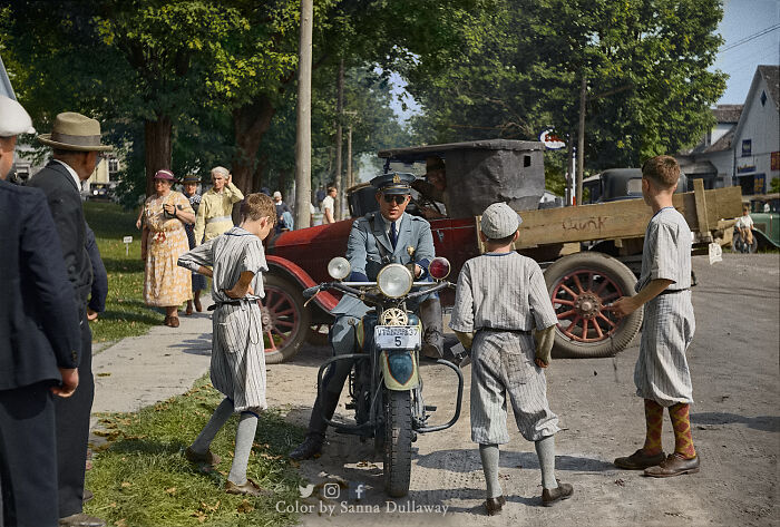 Police officer on a motorcycle talking to boys in vintage baseball uniforms in an interesting colorized history pic.