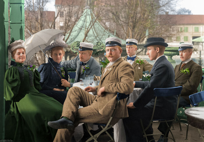 Group of young people dressed in early 20th century fashion sitting outdoors in an interesting colorized history pic.