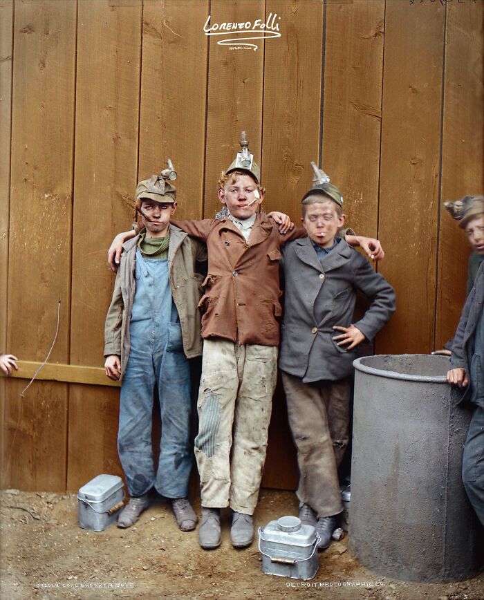 Three young coal miners posing in front of a wooden fence wearing dirty work clothes in colorized history pics.