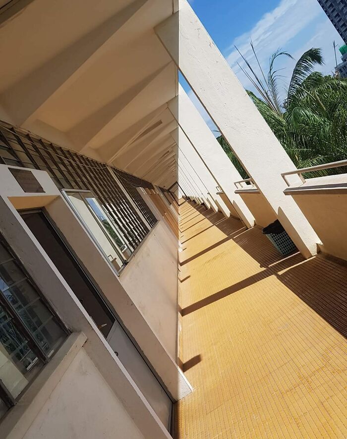Shadows creating geometric patterns along a sunlit corridor with yellow tiled floor and white pillars.