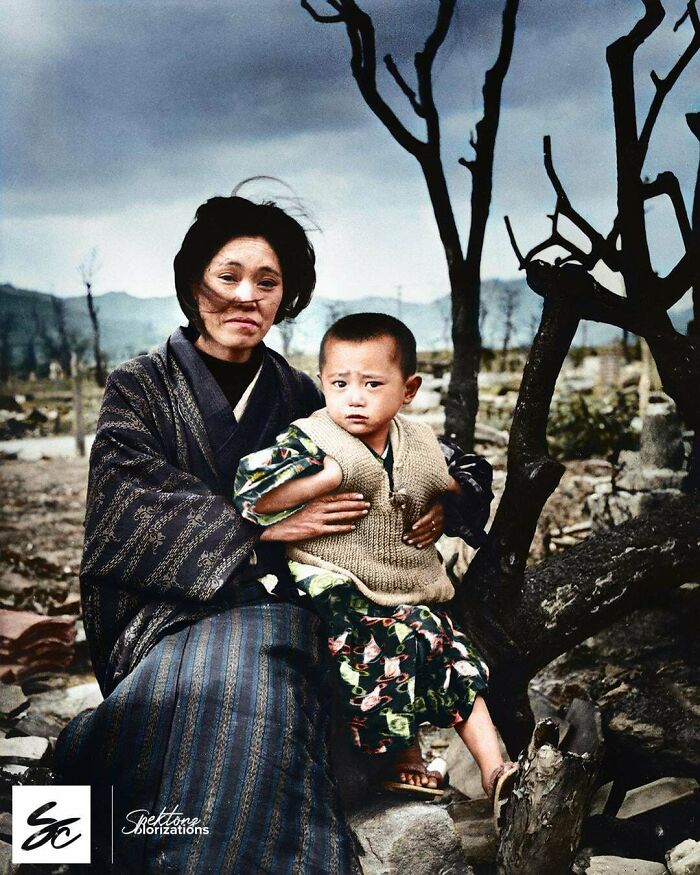 Woman holding child sitting by a barren tree in a desolate area, an interesting colorized history pic from the past.