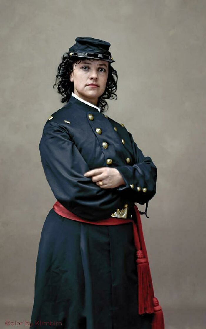 Woman in a dark Civil War uniform with a red sash, arms crossed, in an interesting colorized history pic.