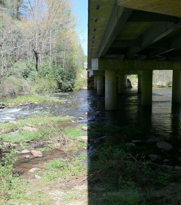 Shadow cast by bridge creates a sharp contrast between light and dark over a riverbank, showing cool and interesting shadows.