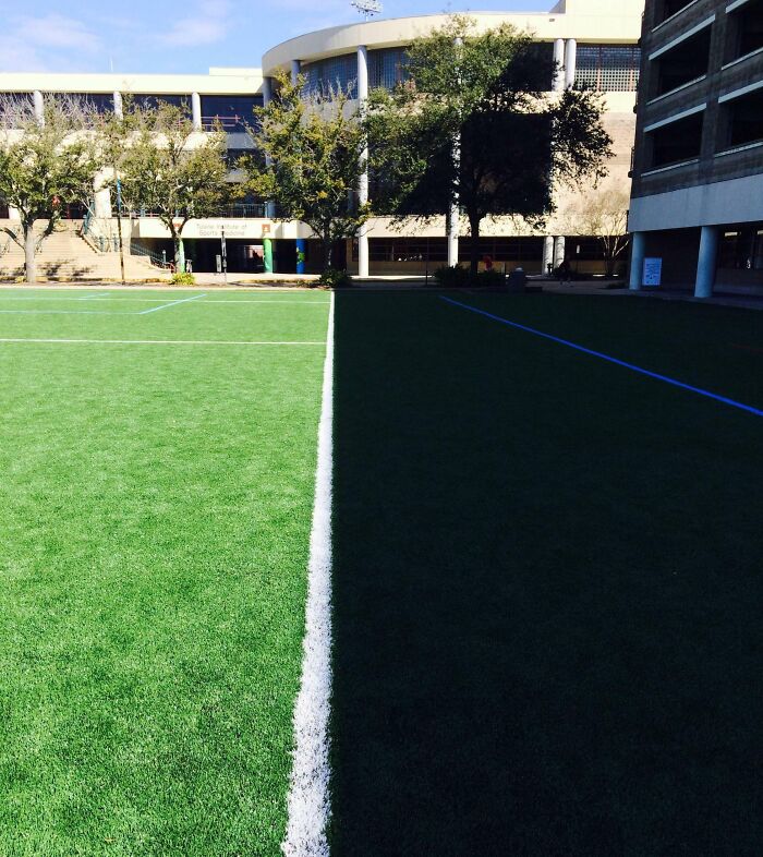 Shadow dividing a green sports field in half with contrasting light and dark areas creating an interesting shadow effect