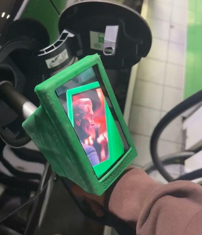 Close-up of a person holding a fuel pump screen displaying an image, symbolizing traumatizing the next generation.