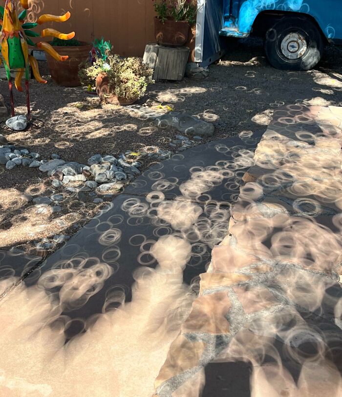 Circular light patterns created by cool and interesting shadows cast on a stone and gravel garden pathway.