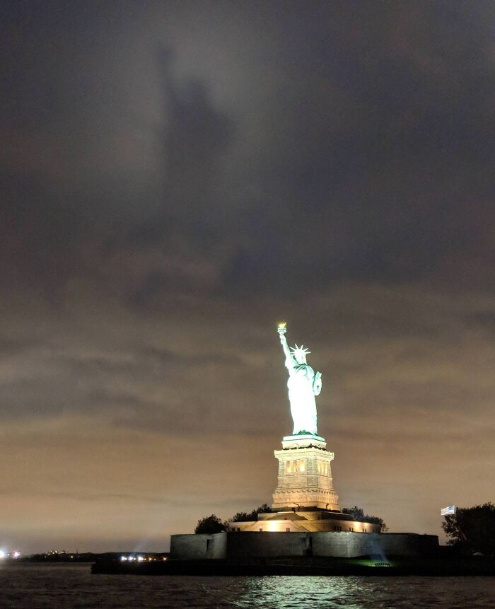 Statue of Liberty illuminated at night with an unusual shadow visible in the cloudy sky, a cool and interesting shadow effect.