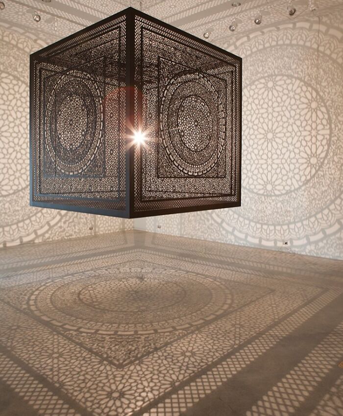 Intricate cube casting cool and interesting shadows on walls and floor in a bright, minimalist room.