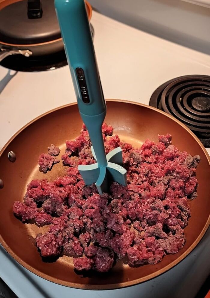 Electric kitchen meat chopper breaking up ground beef in a copper nonstick frying pan on stove.