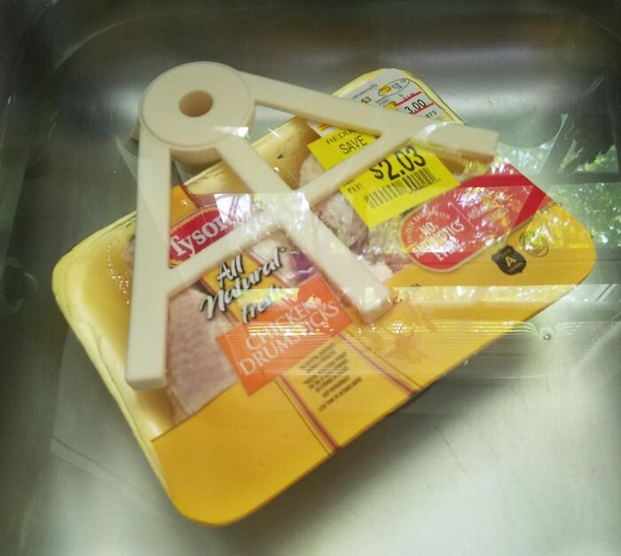 Plastic chicken holder placed on packaged raw chicken in a sink, showcasing best-selling kitchen items.