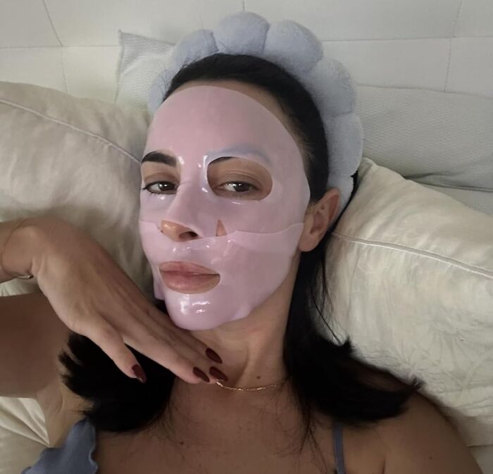 Woman wearing a pink face mask and headband, relaxing on a couch showcasing Amazon's most wished for skincare item.