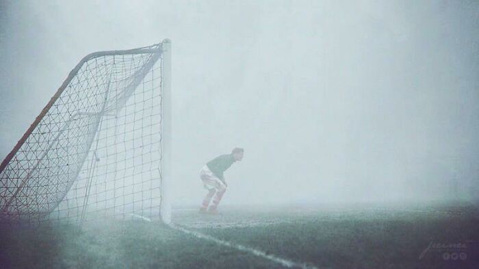 Goalkeeper standing near a soccer net on a foggy field, shown in an interesting colorized history pic.