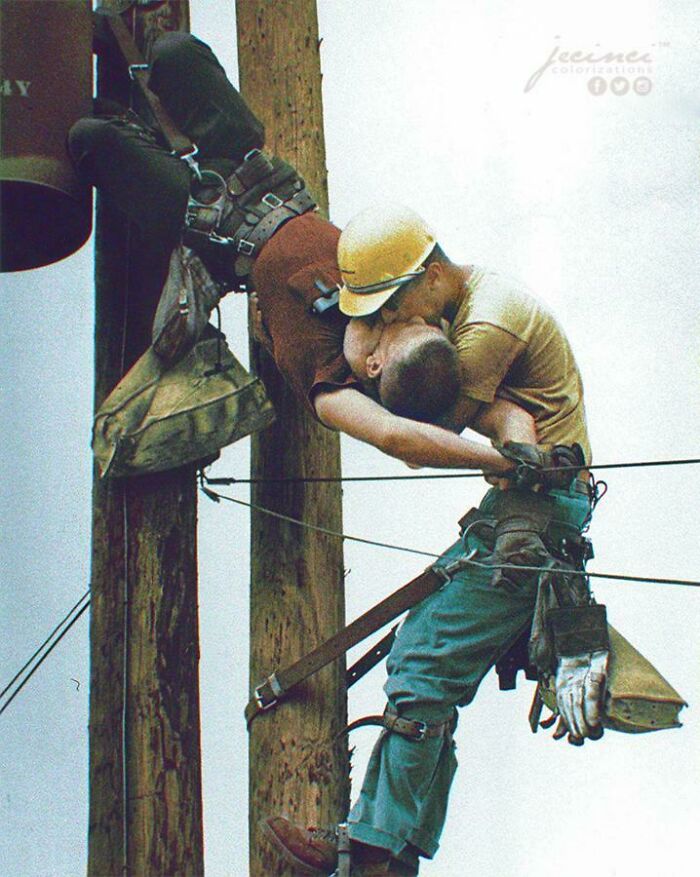 Two utility workers share a kiss high on a pole in this interesting colorized history pic showing a dramatic rescue.